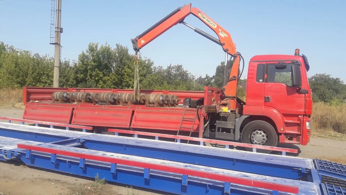 Автомобільні Ваги Grip Line синього кольору поряд червоною вантажівкою зі стрілою-маніпулятором на одному з аграрних підприємств.